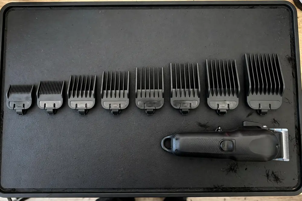 Full set of clipper guard sizes laid out from smallest to largest next to a cordless clipper on a barber station mat